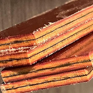 Puede incluir: Primer plano de tres piezas de madera contrachapada con una chapa de color marrón rojizo. La madera contrachapada está formada por finas tiras de madera, creando un patrón a rayas.