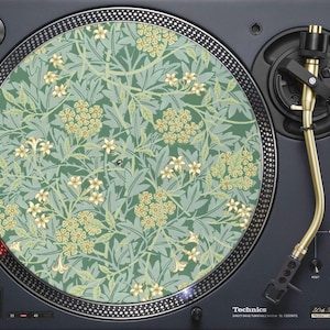 May include: A black turntable with a gold tone arm and a green and yellow floral patterned slipmat. The turntable has a silver control panel with the text "Technics Direct Drive Turntable System SL-1200MK7L 50th Anniversary" printed on it.
