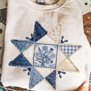 May include: Cream-colored sweatshirt with a star-shaped patchwork design. The star features denim, floral, and gingham fabrics, with a central square showcasing a blue floral illustration. The words "DO NOT COPY" are printed on the design.