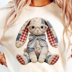 Op de afbeelding: Een handgemaakte patchwork konijnenpop gemaakt van bloemen-, denim- en ginghamstoffen. Het konijn draagt een ronde bril en een blauwe gingham strik. De oren en voeten zijn afgewerkt met rood-wit gingham. Een grillig decoratief item met Pasen- of lentethema.