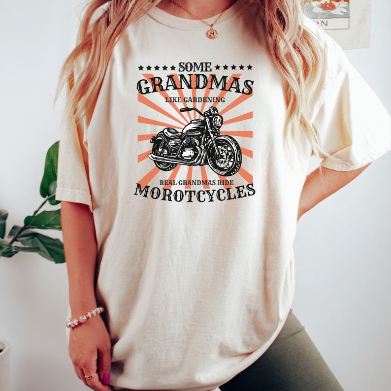 May include: A white t-shirt with a black and white illustration of a motorcycle. The text on the shirt reads "Some Grandmas Like Gardening Real Grandmas Ride Motorcycles".
