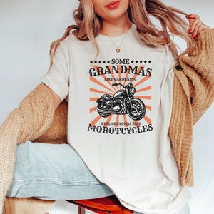 May include: A white t-shirt with a graphic design featuring a motorcycle and the text "Some Grandmas Like Gardening Real Grandmas Ride Motorcycles".