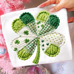 Puede incluir: Aplicación de trébol hecha a mano en tonos verdes y blancos. El trébol presenta un borde tejido y está decorado con pequeños motivos de tréboles y corazones. El diseño incluye varias texturas y patrones, con detalles de purpurina en el centro.