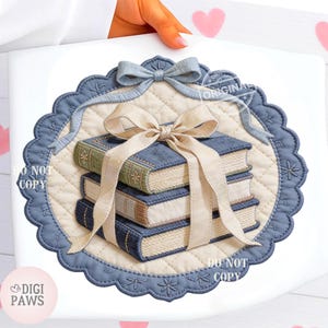 May include: A quilted, cream-coloured mat with a blue scalloped border and a stack of books. The books are blue with gold accents and tied with a cream-coloured ribbon and a blue bow. The words "DO NOT COPY" and "ORIGINAL" are visible.