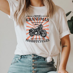 May include: White t-shirt with a black and white illustration of a motorcycle and the text "Some Grandmas Like Gardening Real Grandmas Ride Motorcycles".