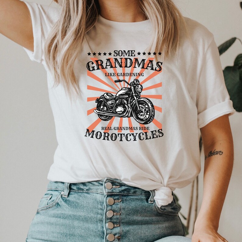 May include: White t-shirt with a black and white illustration of a motorcycle and the text "Some Grandmas Like Gardening Real Grandmas Ride Motorcycles".