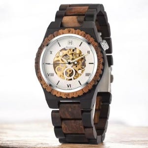 May include: A wooden wristwatch with a visible mechanical movement. The watch features a light-colored face with Roman numerals and the brand name "Bosni". The band and bezel are made of dark and light brown wood.