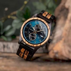 Peut inclure: Une montre-bracelet en bois avec un bracelet noir et bois et un cadran bleu et noir. Le cadran de la montre comporte plusieurs cadrans et la marque "BOBOBIRD". La montre a une lunette en bois sur un fond flou.