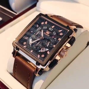 Puede incluir: Un reloj OLEVS rectangular con una correa de cuero marrón. La esfera del reloj es negra con detalles dorados y tres subesferas. El reloj tiene un bisel y una corona dorados. El reloj se muestra en una caja blanca.