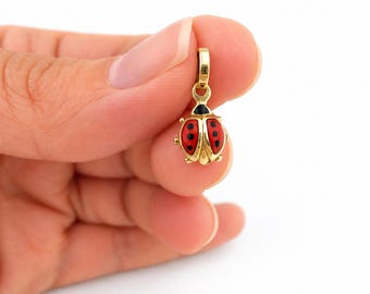 Könnte beinhalten: Ein goldener Anhänger in Form eines Marienkäfers mit poliertem Gelbgold-Finish, ausgestattet mit leuchtend roten Emaille-Flügeln, die mit kleinen schwarzen Punkten akzentuiert sind, und einem schwarzen Emaille-Kopf sowie einer kleinen Öse.