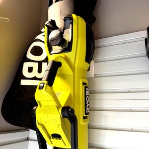 May include: A yellow and black Ryobi leaf blower with a black collection bag. The blower is mounted on a white wall. The Ryobi logo is visible on the side of the blower.