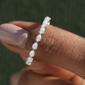 Puede incluir: Un anillo de plata con una banda de diamantes en forma de pera. El anillo está en un dedo.