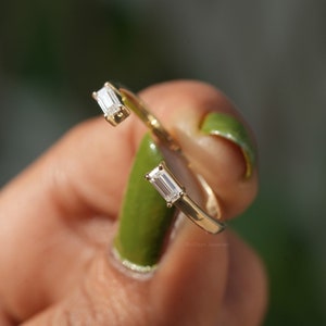 Puede incluir: Un anillo de oro con dos diamantes de forma baguette. El anillo está retorcido y los diamantes están engastados en garras.