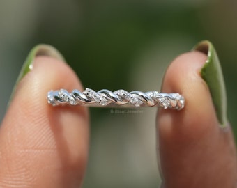Puede incluir: Un anillo de banda de plata con un diseño trenzado y pequeños diamantes engastados en el metal. El anillo está siendo sostenido por un dedo.