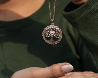 May include: A rose gold necklace with a tree of life pendant featuring a heart at the center. The pendant is surrounded by a delicate filigree design and has small clear stones set into the leaves.