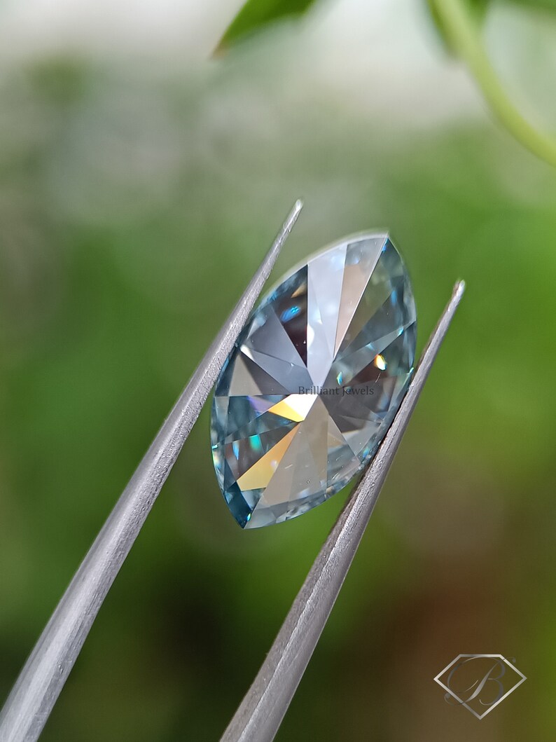 May include: A light blue marquise cut gemstone held by tweezers against a green background. The gemstone has a brilliant cut and facets that reflect light.