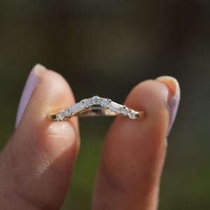 Puede incluir: Un anillo de banda de oro con un diseño de chevron con diamantes baguette y redondos.