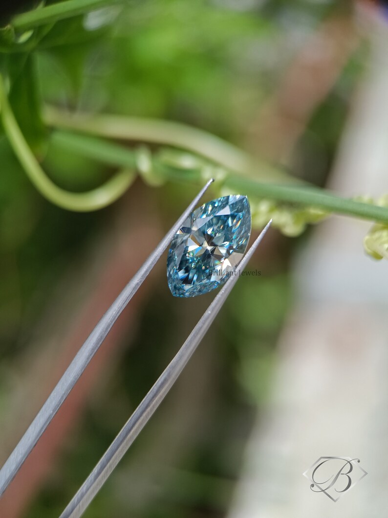 May include: A light blue marquise cut diamond held by tweezers against a green leafy background.  Brilliant Jewels is visible in the image.