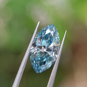 May include: A light blue, faceted, oval-shaped diamond held in tweezers against a green background.
