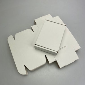 May include: A stack of white cardboard boxes, some folded flat and some assembled, with a single box standing upright on top.