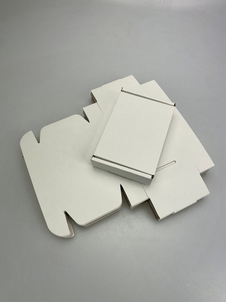 May include: A stack of white cardboard boxes, some folded flat and some assembled, with a single box standing upright on top.