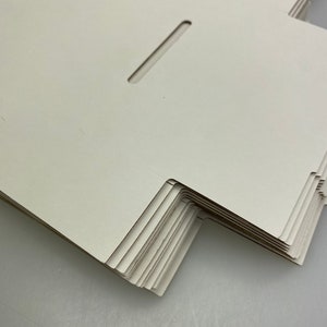 May include: A stack of white cardboard boxes with a cut-out slot on the top of each box.