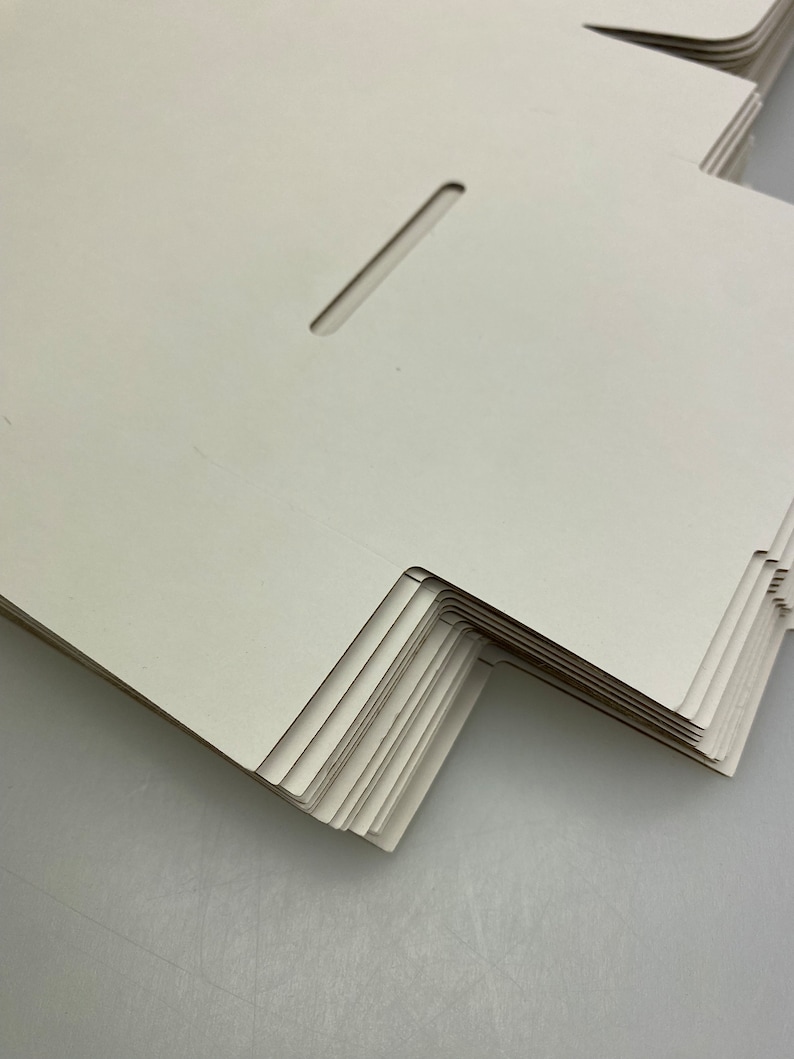 May include: A stack of white cardboard boxes with a cut-out slot on the top of each box.