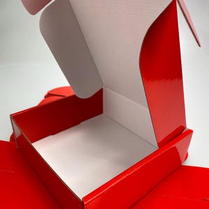 Peut inclure: Une boîte en carton rouge avec un intérieur blanc. La boîte est ouverte et le couvercle est rabattu.