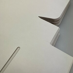 May include: A stack of white cardboard boxes with a cut-out slot on the side. The boxes are folded and ready to be assembled.