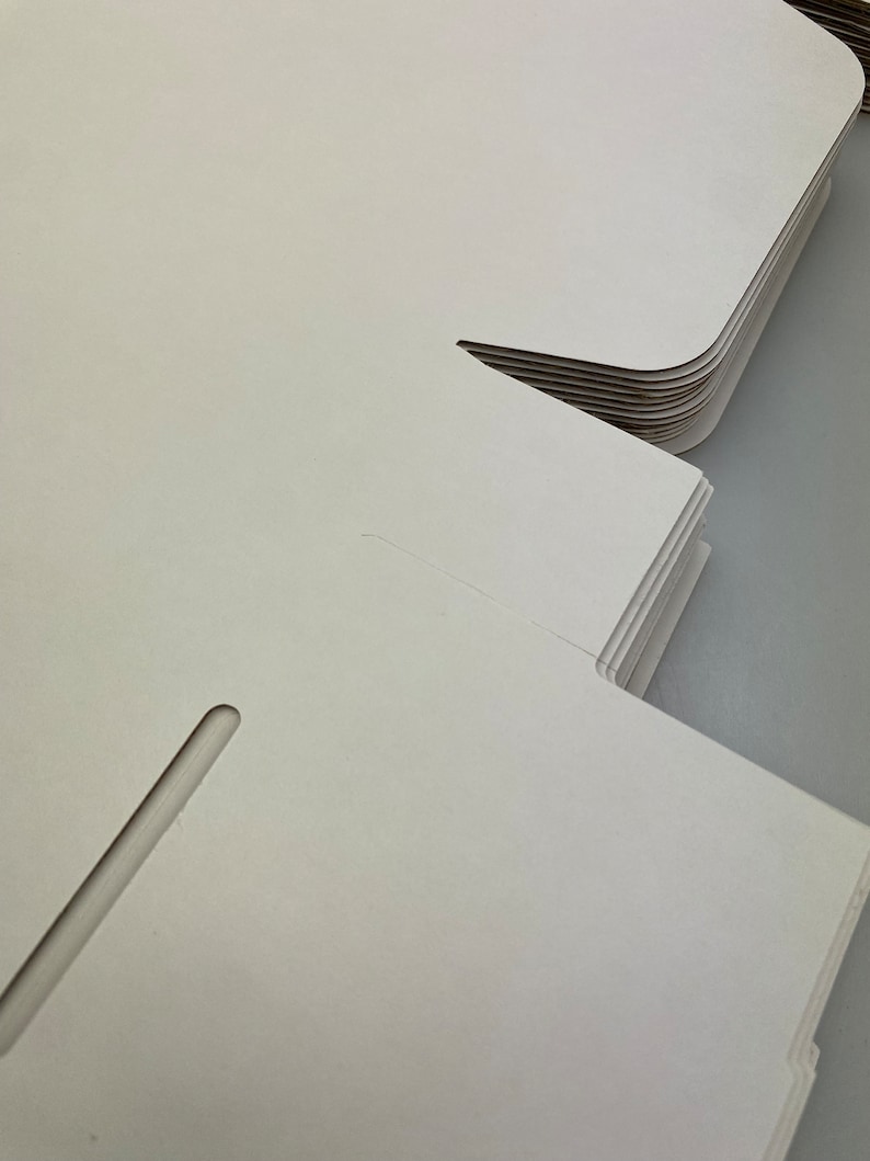 May include: A stack of white cardboard boxes with a cut-out slot on the side. The boxes are folded and ready to be assembled.