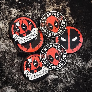 May include: Four round black and red coasters with a Deadpool character design. The coasters feature the text "I'm Sorry. Did I Offend You?" and "I'm a Unicorn".