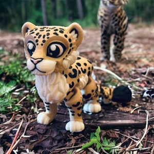 Könnte beinhalten: Eine kleine, handbemalte Figur eines Leoparden mit schwarzen Flecken auf einem braunen Hintergrund. Die Figur hat große, cartoonartige Augen und eine flauschige weiße Mähne. Sie steht auf einem Bett aus braunen Blättern und Zweigen.