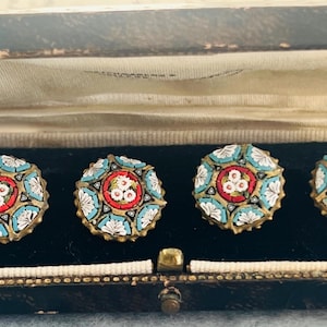 May include: A set of four round cufflinks featuring intricate micro-mosaic floral patterns in shades of turquoise, white, and red, set within a gold-toned metal frame. The cufflinks are displayed in a rectangular, dark brown hinged storage box.