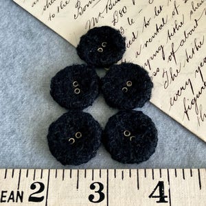 May include: Five dark navy blue, round fabric buttons with two small holes each. The buttons are arranged in a cluster on a light grey surface, with a vintage handwritten letter in the background. A ruler is at the bottom.