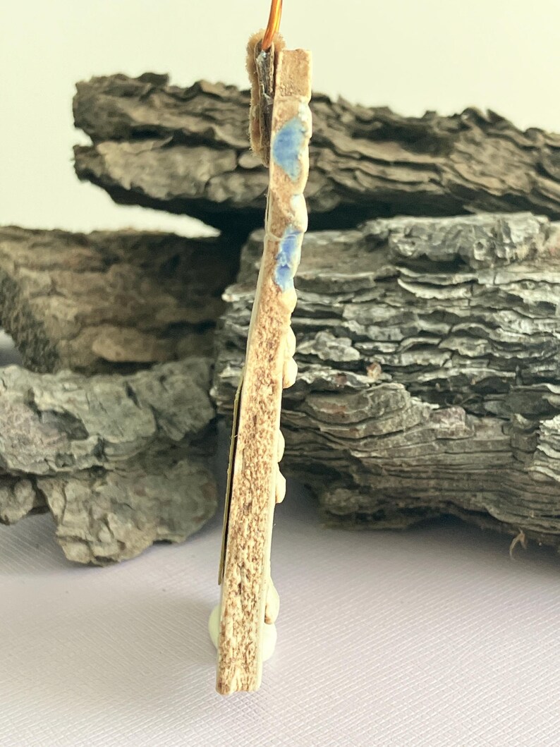 May include: A ceramic pendant with a brown and white glaze and blue accents. The pendant is shaped like a rectangle with rounded corners and has a hole at the top for hanging.