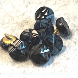 May include: A cluster of round, black buttons featuring a faceted surface with geometric, etched line patterns. Each button has a metallic gold-toned shank on the back for attachment, and the dark, reflective material creates a high-contrast appearance.