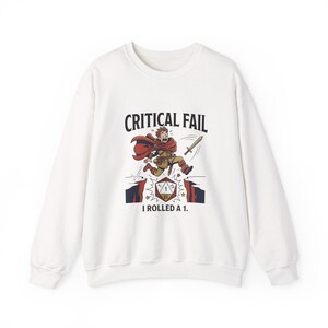 May include: White sweatshirt with a graphic of a cartoon character running with a sword, labeled "CRITICAL FAIL" and "I ROLLED A 1." The character wears a red cape and brown clothing. The design is in a comic book style.
