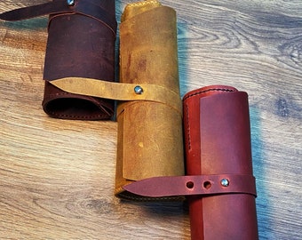 May include: Three leather rolls in different colors: brown, yellow, and red. Each roll has a strap with a metal buckle.