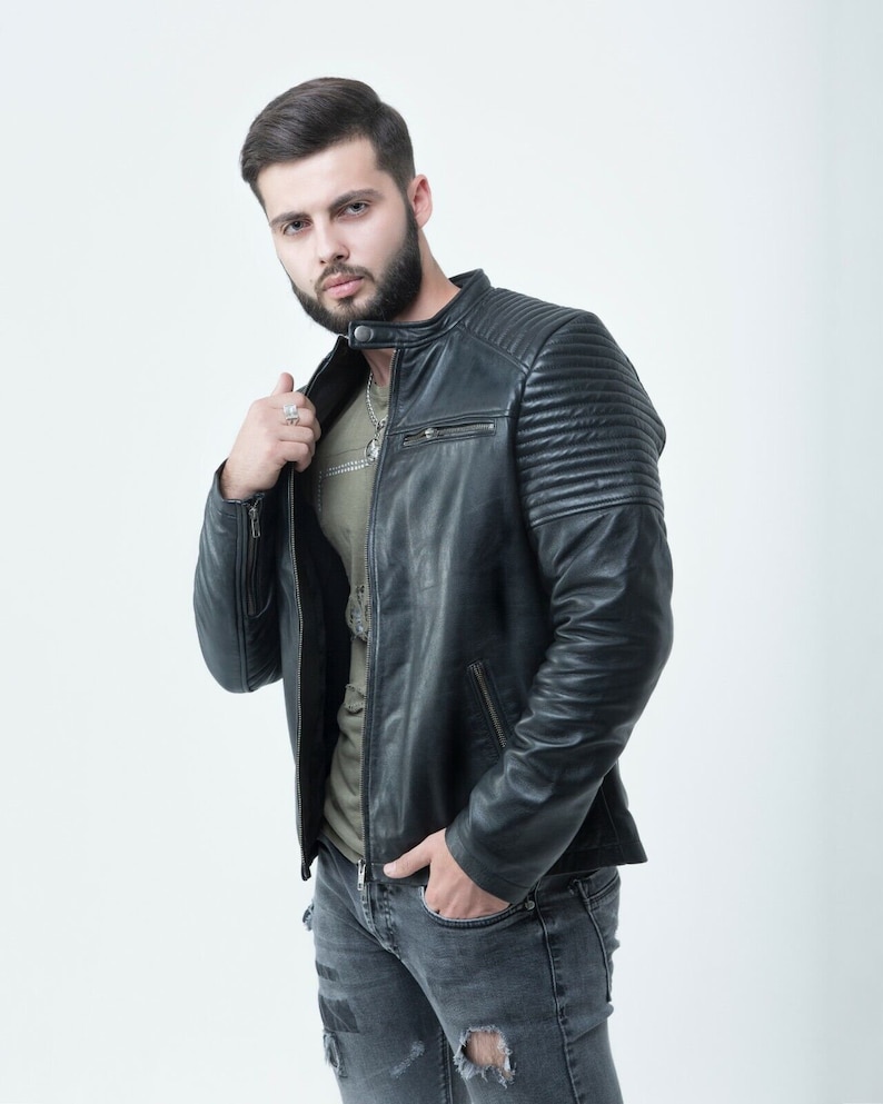 Peut inclure: Un homme portant une veste en cuir noire avec une fermeture &eacute;clair et un t-shirt vert en dessous. Il porte un jean bleu avec des d&eacute;tails us&eacute;s.