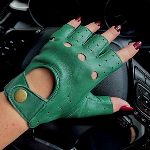 Op de afbeelding: Groene leren rijhandschoenen met een vingerloos ontwerp en een gouden knoopsluiting. De handschoenen hebben een geperforeerd patroon en worden op een hand getoond.