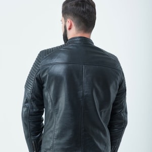 Peut inclure: Une veste en cuir noire avec un design matelass&eacute; sur les &eacute;paules et les manches. La veste a une fermeture &eacute;clair et un col montant.