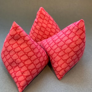 May include: Three pink fabric triangular cushions with a geometric pattern. The cushions are arranged in a triangular shape.