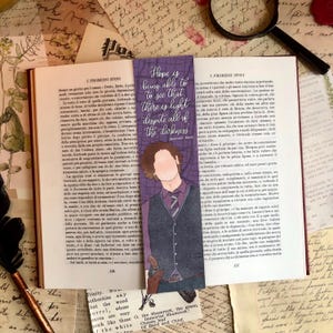 May include: A bookmark with the text "Hope is being able to see that there is light despite all of the darkness" and an illustration of a person. The bookmark is placed in an open book.