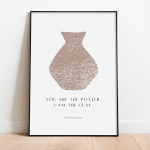Op de afbeelding: Een ingelijst print met een beige vaasillustratie en de tekst "Jij bent de pottenbakker. Ik ben de klei." Jesaja 64:8.