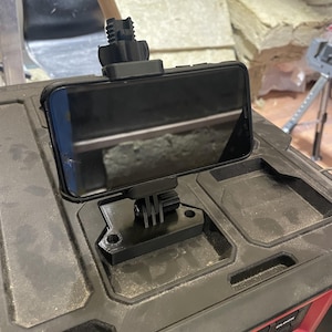 May include: A black phone mounted on a black phone holder with a GoPro mount. The phone is mounted on a black toolbox with red accents.
