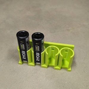 May include: A lime green 3D-printed battery holder with two black and yellow Ryobi USB Lithium batteries inserted. The holder has three slots for batteries and is designed to keep them organized.