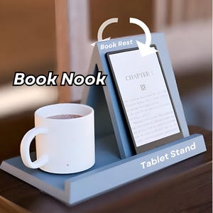 Op de afbeelding: Een blauwe houten standaard met een boekenlegger, een tabletstandaard en een bekerhouder. De standaard is gelabeld met "Book Nook", "Book Rest" en "Tablet Stand".