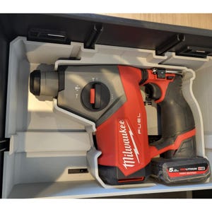May include: A red and black Milwaukee FUEL M12 hammer drill in a grey case. The drill has a grey head, a red body with the Milwaukee logo, and a black battery pack. The case is open, revealing the drill's shape.