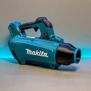 Puede incluir: Un soplador de hojas inalámbrico Makita, de color turquesa y negro. Tiene un mango curvo y una boquilla. El logotipo de Makita es prominente. Diseñado para soplar hojas y escombros.