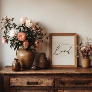 以下が含まれることがあります： 「as for me and my house, we will serve the Lord」という言葉が書かれた木製のフレームプリントが、木製のドレッサーの上に置かれています。ピンクのシャクヤクが入った大きな花瓶と、他の花瓶がドレッサーの上にあります。